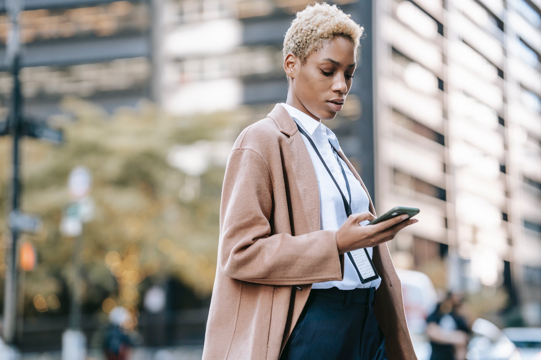focused black businesswoman browsing smartphone on urban street