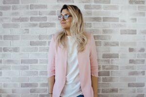 woman in pink cardigan and white shirt leaning on the wall